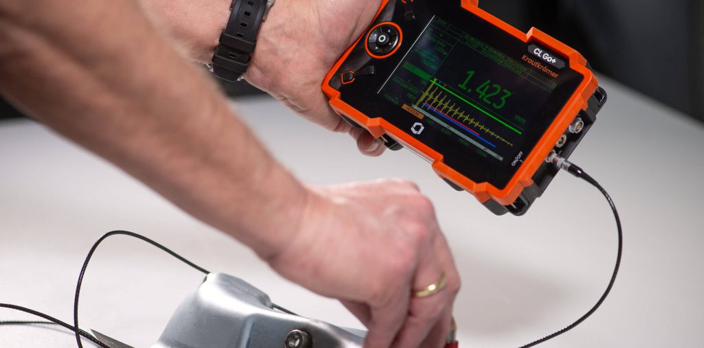 技術(shù)人員使用Krautkr?mer CL Go+超聲波精密測(cè)厚儀對(duì)金屬部件進(jìn)行厚度測(cè)量，顯示屏實(shí)時(shí)顯示測(cè)量結(jié)果，適用于工業(yè)無(wú)損檢測(cè)。