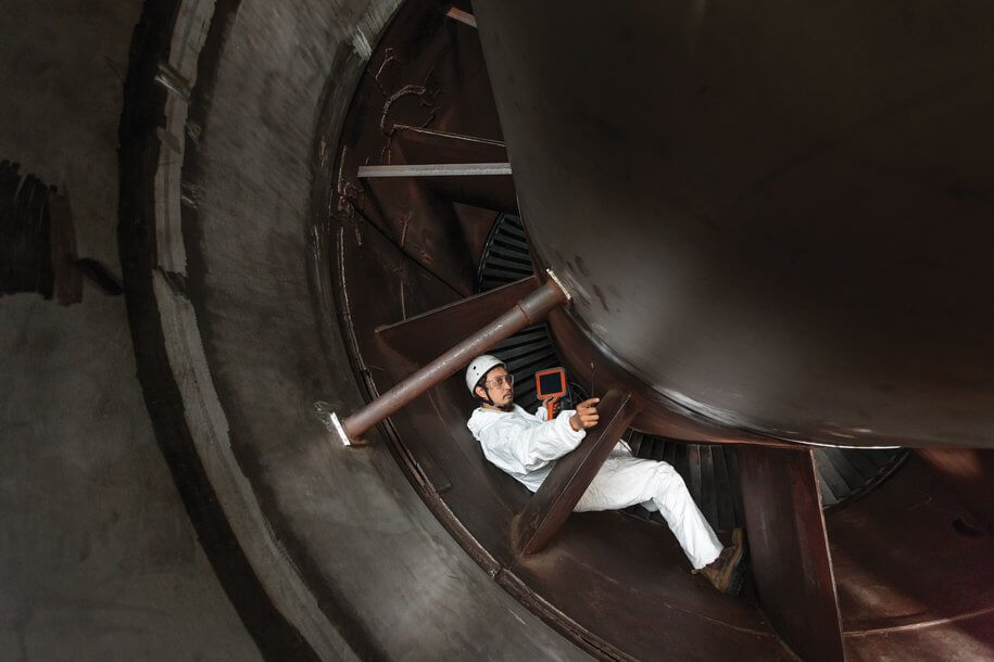 一位穿著安全裝備的技術(shù)人員在工廠中使用手持工具檢查渦輪發(fā)動(dòng)機(jī)，旁邊另一名工人拿著平板設(shè)備，展現(xiàn)工業(yè)維護(hù)和檢測(cè)場(chǎng)景。