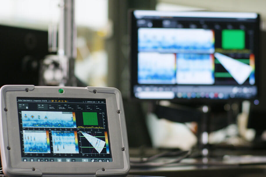 一名穿著灰色襯衫的技術(shù)人員在明亮的工業(yè)環(huán)境中指向平板屏幕，屏幕顯示聲吶成像數(shù)據(jù)，平板放置在堅固外殼上，旁邊有一根圓柱形工具。