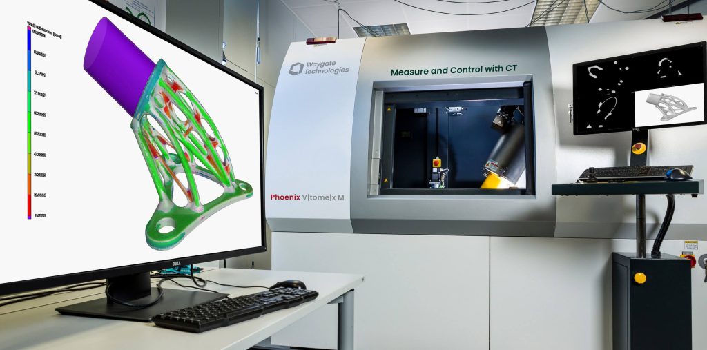 實(shí)驗(yàn)室中Waygate Technologies Phoenix VTomelx M CT機(jī)器的照片，顯示屏上展示掃描對(duì)象的3D彩色模型，桌上有鍵盤和鼠標(biāo)。