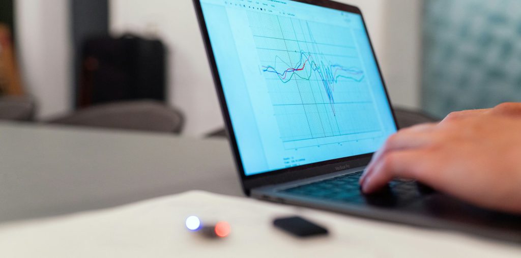 一位工作人員正在使用MacBook Pro筆記本電腦查看傳感器數(shù)據(jù)圖表，圖表顯示多條顏色不同的折線，代表工業(yè)或科研數(shù)據(jù)分析過(guò)程，桌面上有一個(gè)激光筆和一個(gè)黑色USB設(shè)備。