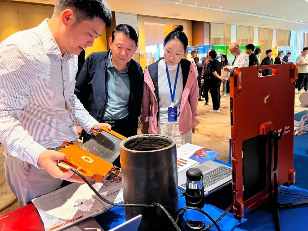 Waygate Technologies工程師在展會上向參觀者演示DXR Flex探測器的操作方法，觀眾聚精會神觀看設(shè)備檢測管道樣品。